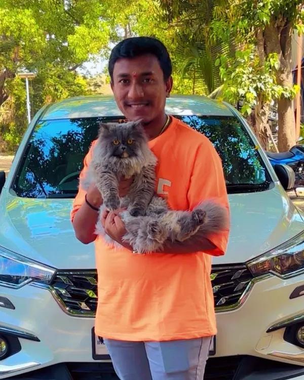 A pet parent holding a fluffy grey Persian cat on a tree-lined street